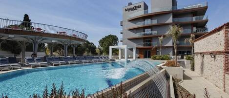 Un hotel moderno con piscina, un paseo cubierto y un edificio de varios pisos con balcones.