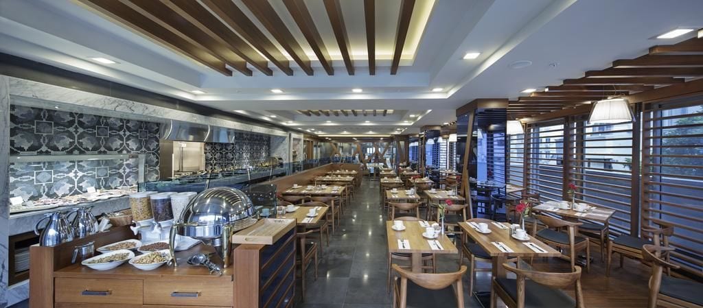 Un interior de restaurante moderno con mesas largas, sillas de madera y una zona de bar central.
