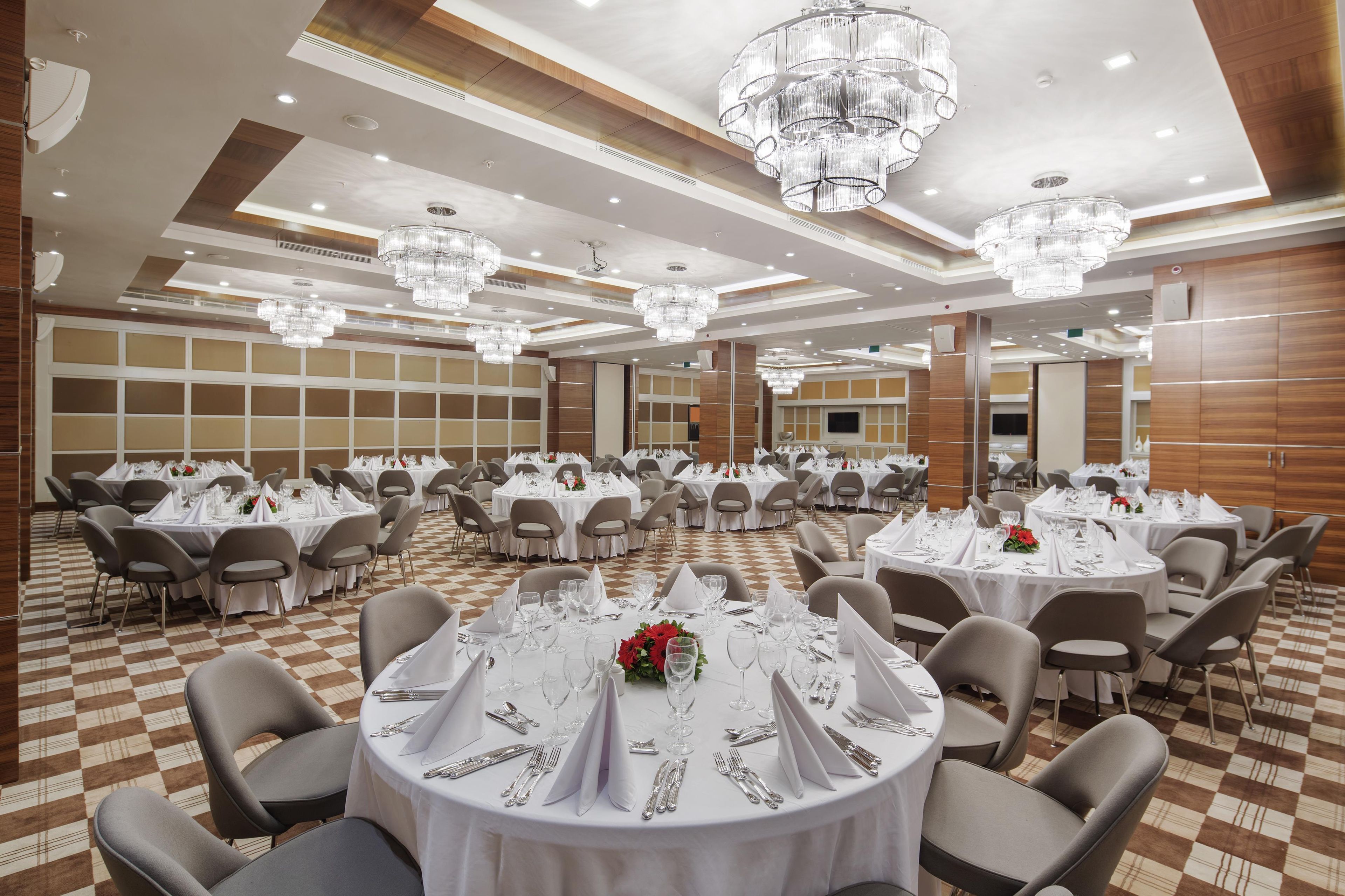 A banquet hall with round tables set for dining, equipped with chairs, and adorned with crystal chandeliers.