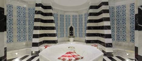 Un baño lujoso con un lavamanos circular de mármol en el centro, paredes a rayas negras y blancas, y azulejos con motivos azules.