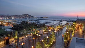 Una terrazza sul tetto con posti a sedere all'aperto, con vista su un porto turistico e sullo skyline cittadino al crepuscolo.