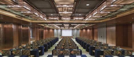 A conference room with rows of tables and chairs, a large screen at the front, and a modern ceiling design.