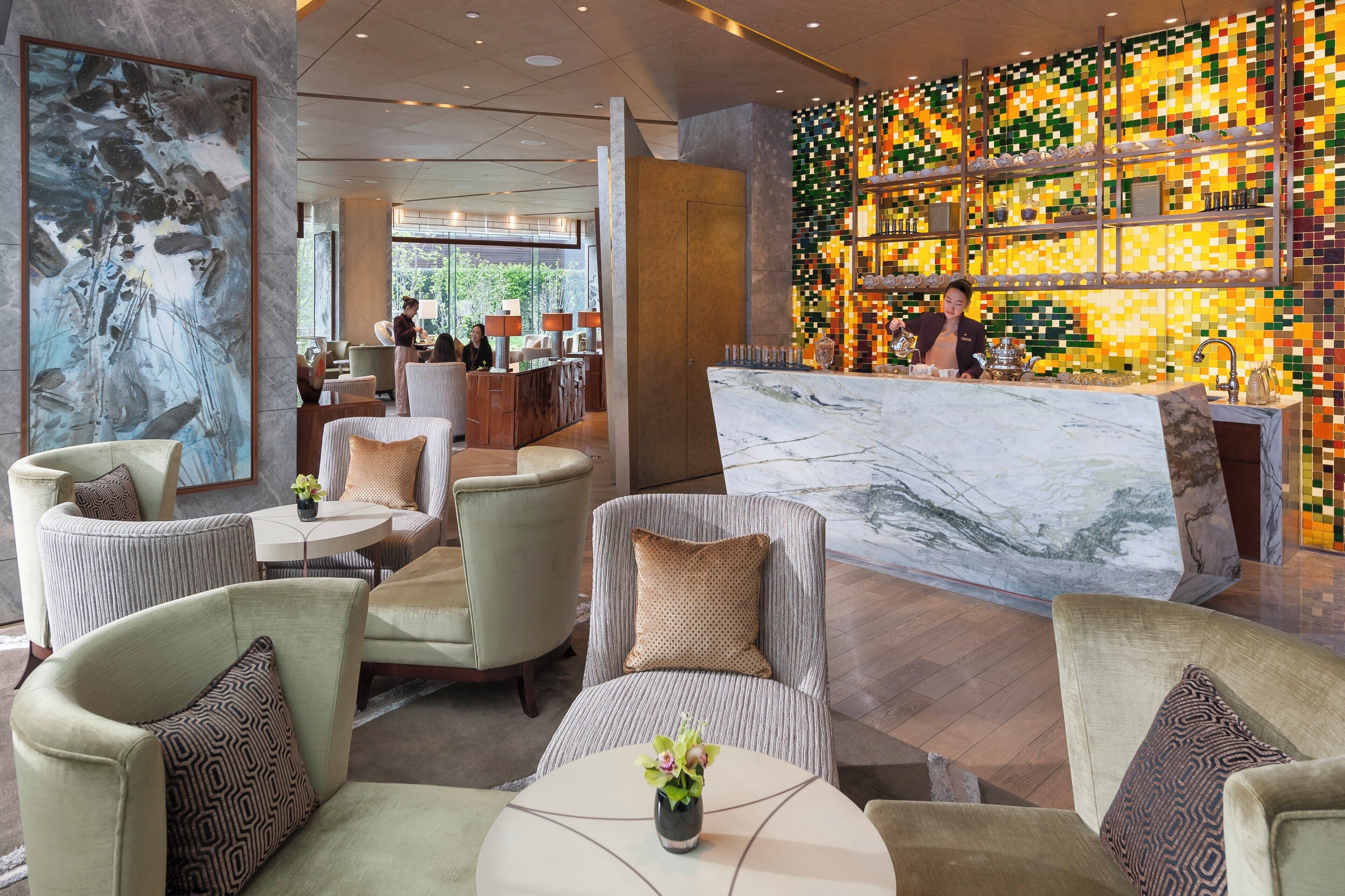 A modern hotel lobby with comfortable seating, a marble reception desk, and a colorful mosaic wall.