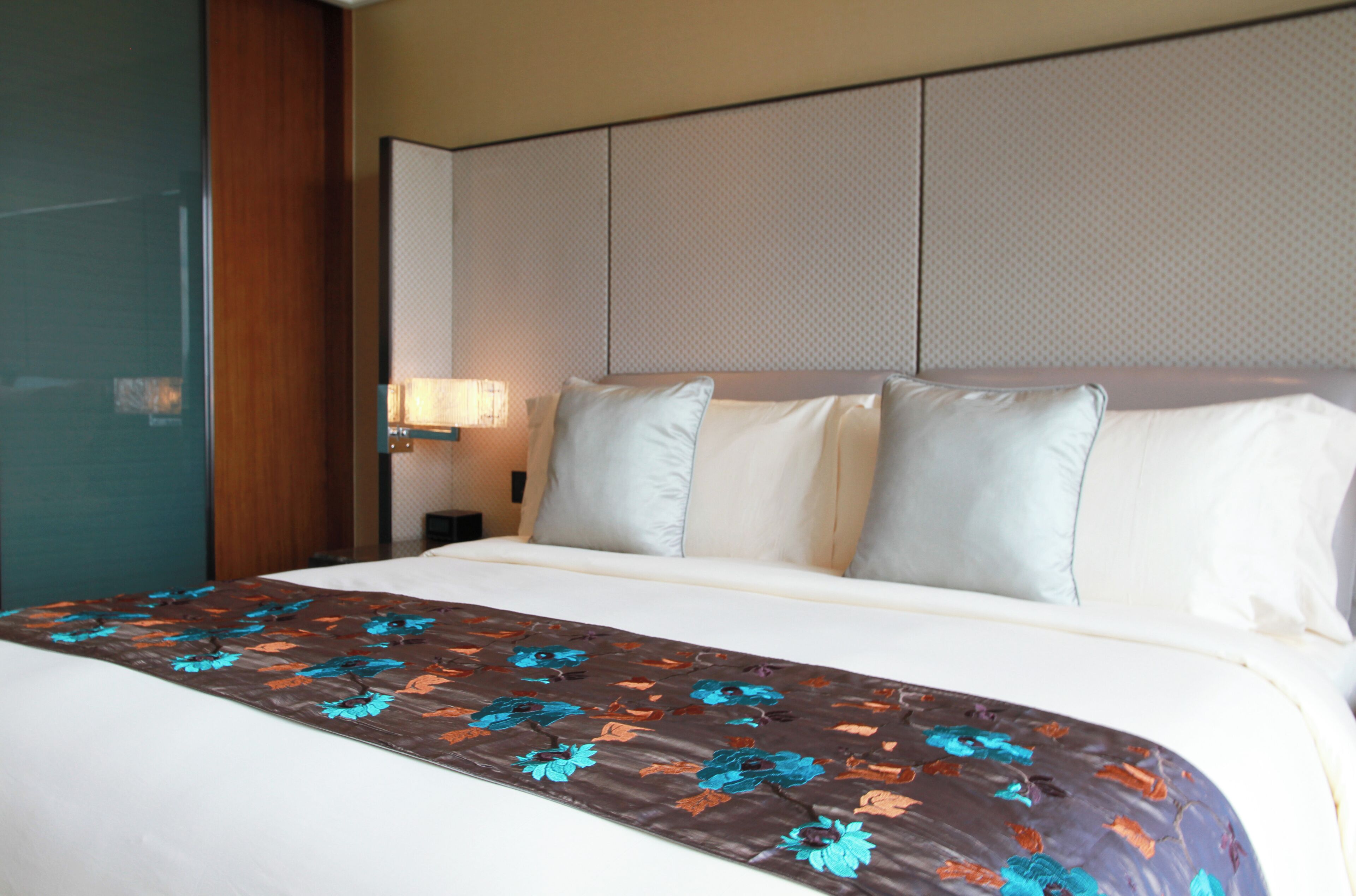 A hotel room with a bed, a nightstand, and a wall-mounted lamp.