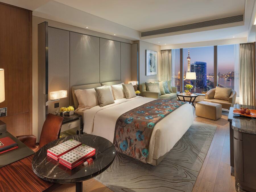 A modern hotel room with a large bed, a desk, a chair, and a TV.