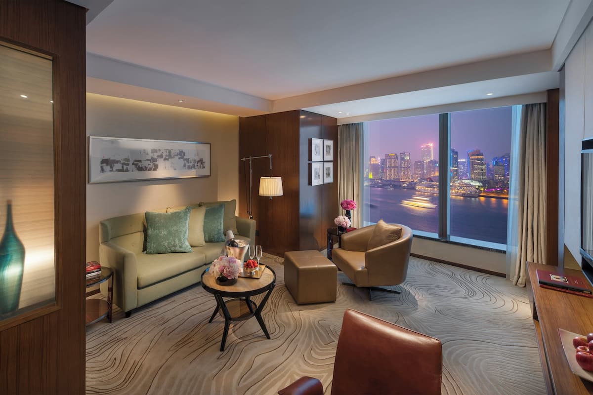 Een moderne hotelkamer met een groot raam dat uitzicht biedt op de stad, een bank, een bijzettafeltje en een televisie.