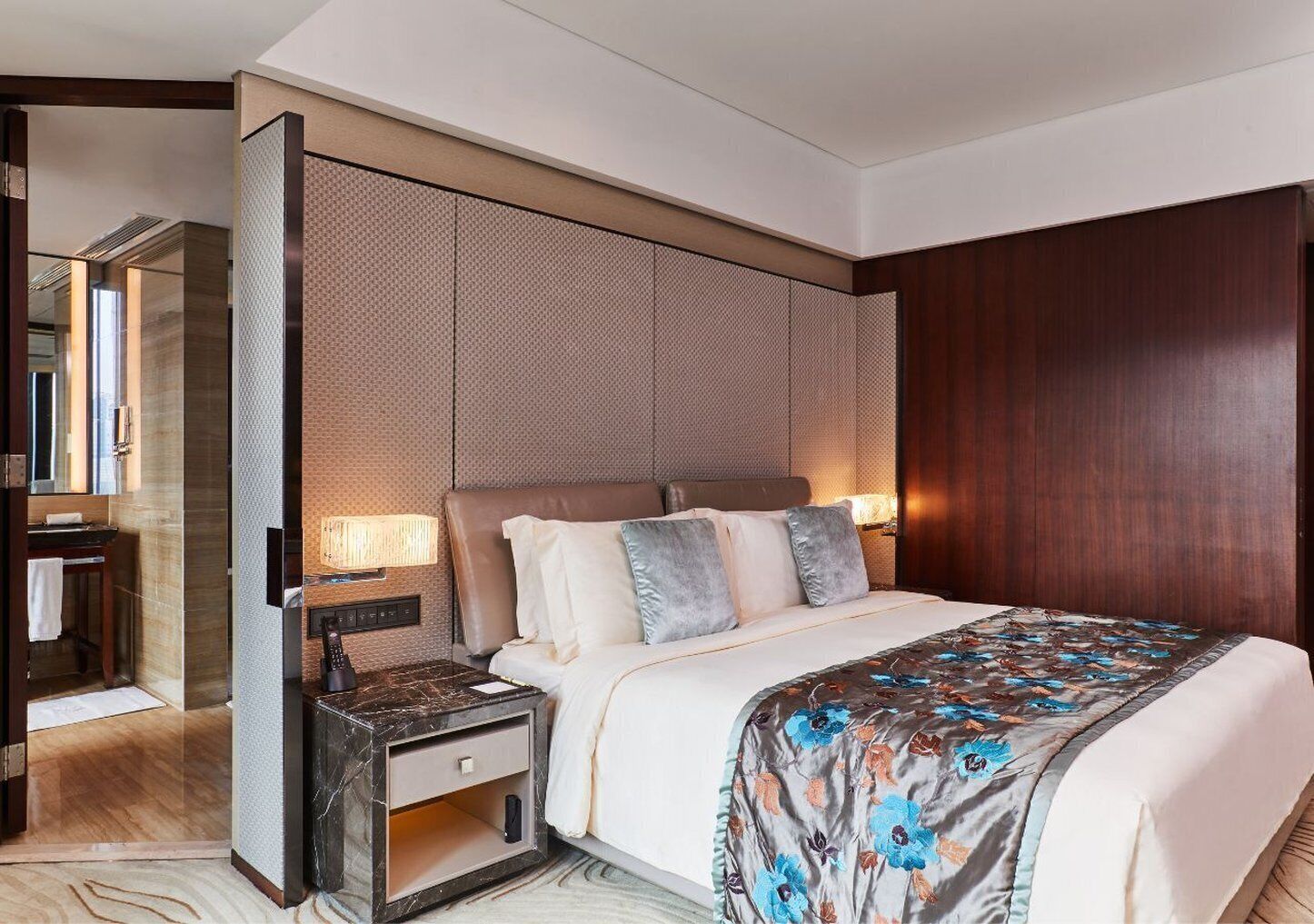 A hotel room with a large bed, a nightstand with a lamp, a wooden headboard, and a large mirror.
