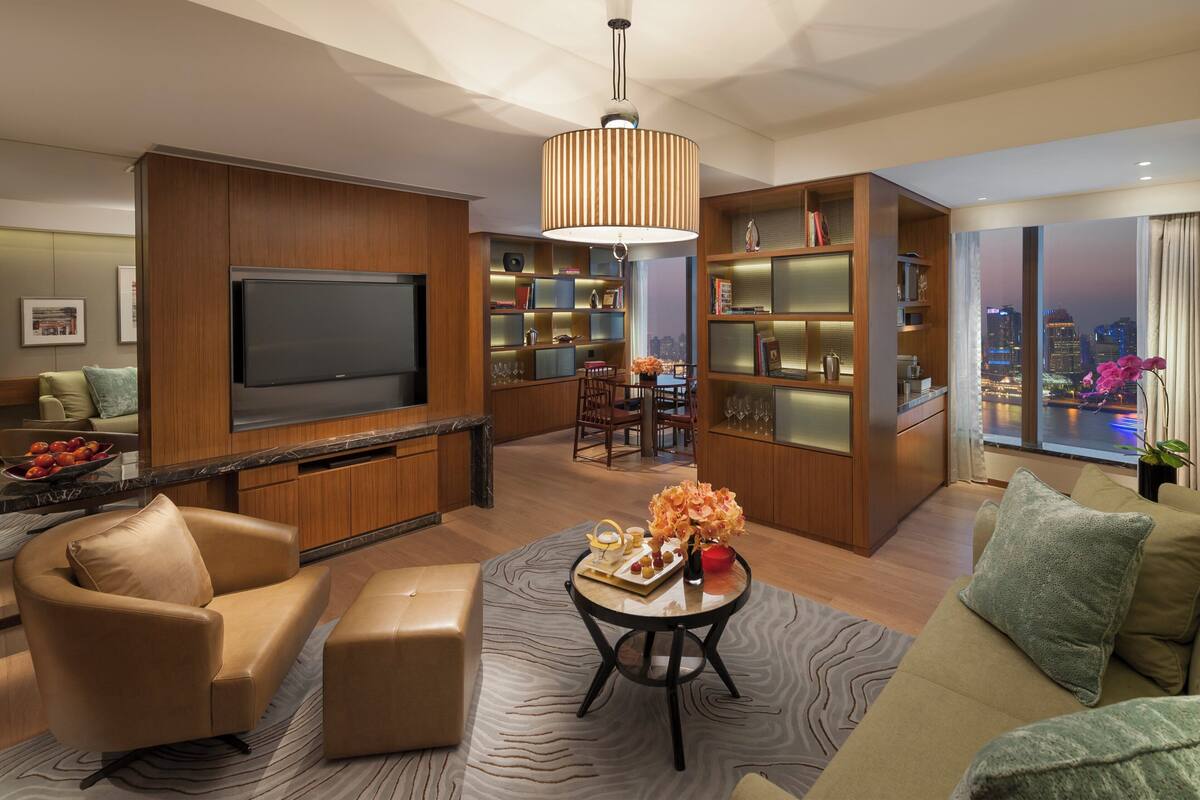 Een moderne woonkamer met een flatscreen televisie, houten kasten, een eethoek en uitzicht op de stad.