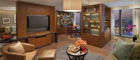 A modern living room with a flat-screen TV, wooden shelving, a dining area, and a view of the cityscape.
