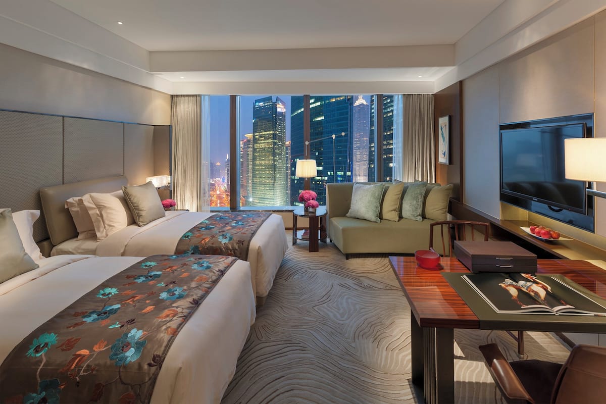 A hotel room with two beds, a sofa, a TV, and a dining table.