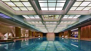 Una amplia piscina interior con techo alto y tragaluces, rodeada de zonas de descanso y una pared de piedra.