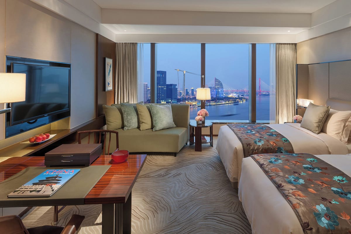 A hotel room with a large bed, a sofa, a TV, and a view of a cityscape.