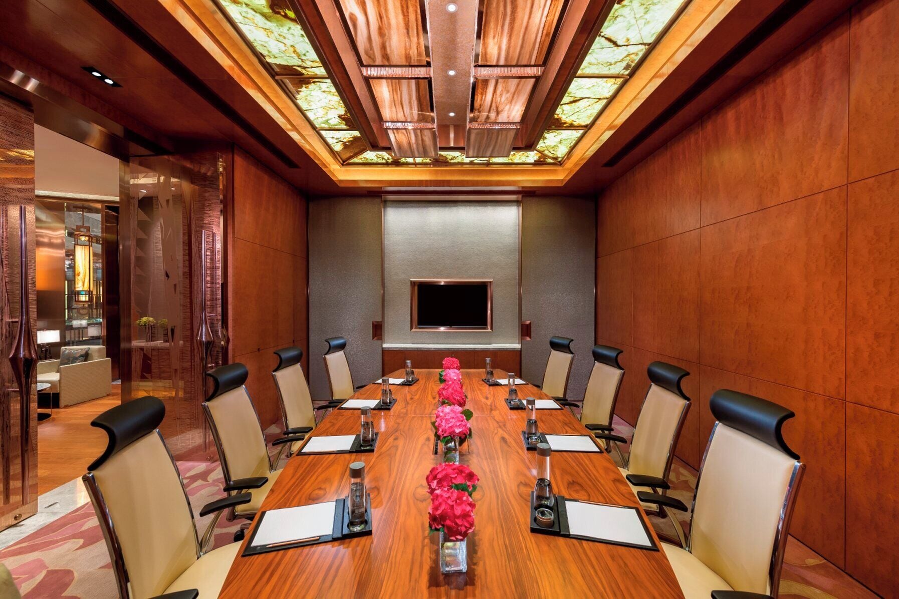 A conference room with a long table, chairs, a flat-screen TV, and a wooden ceiling with skylight.