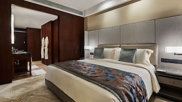 A hotel room with a large bed, a wooden wardrobe, a desk with a chair, and a bathroom visible through an open door.