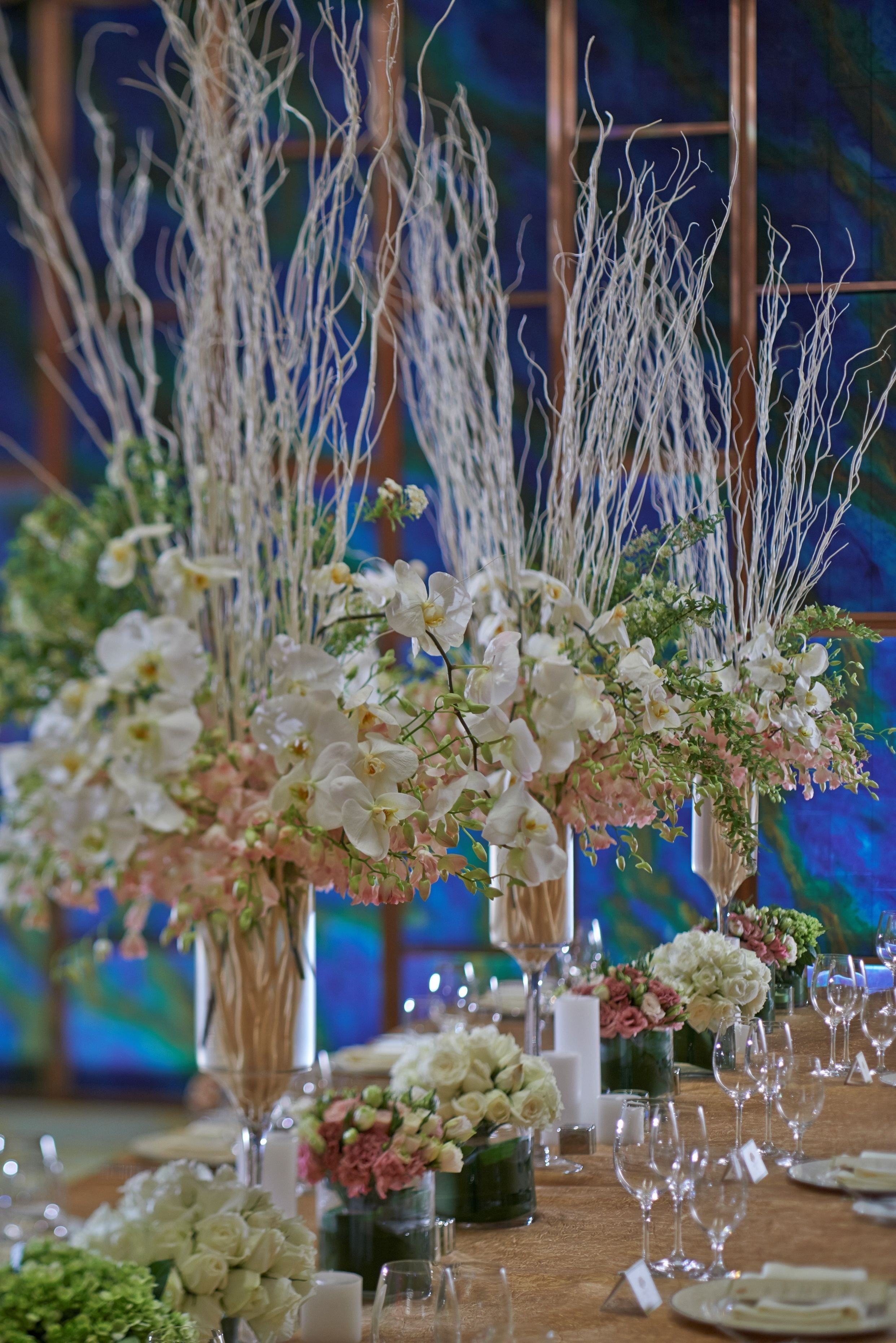 A table set for a formal event with floral centerpieces, clear glassware, and a wooden table surface.