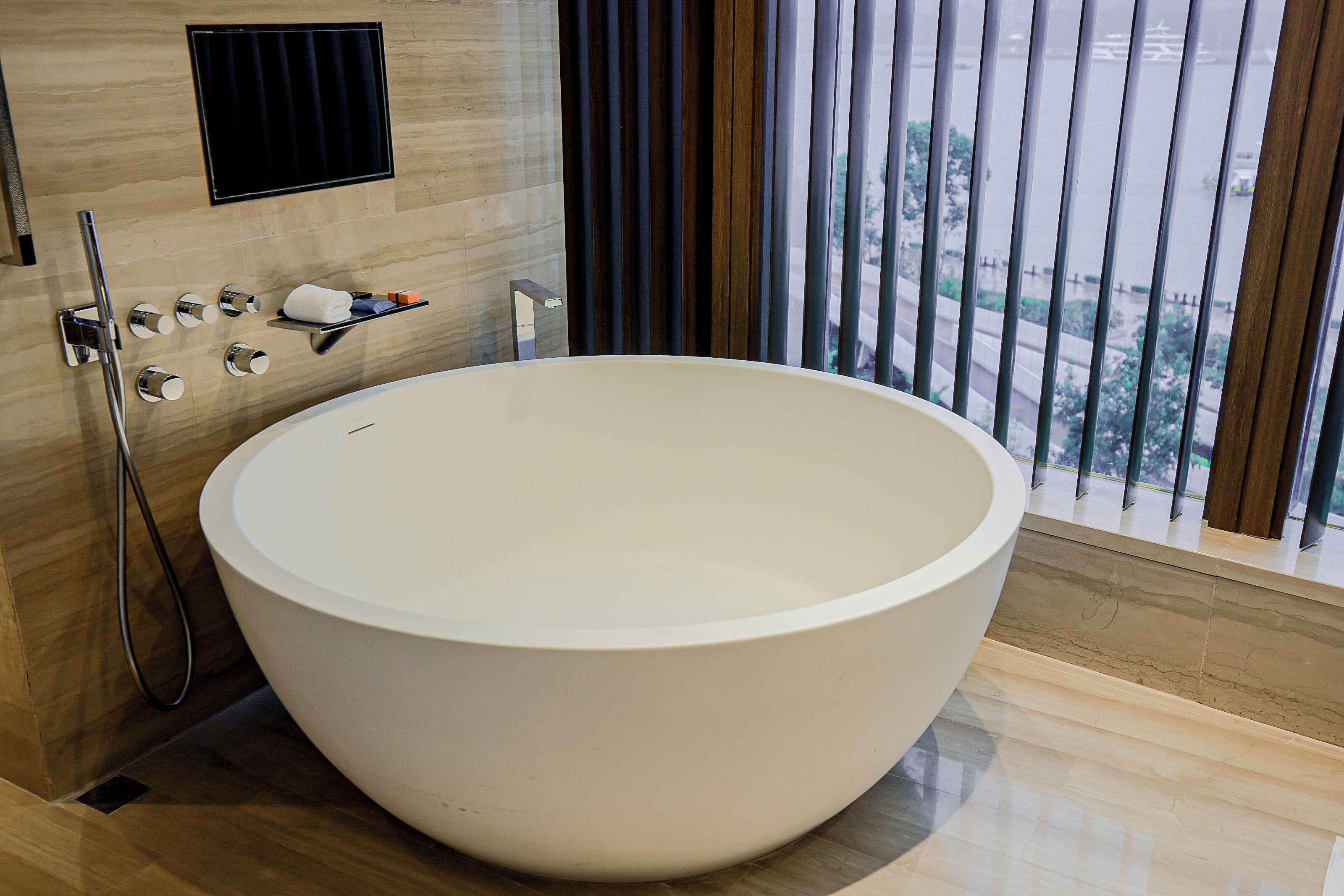 A modern bathroom with a large freestanding bathtub, a shower area, and a window with blinds.