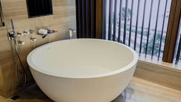 A modern bathroom with a large freestanding bathtub, a shower area, and a window with blinds.