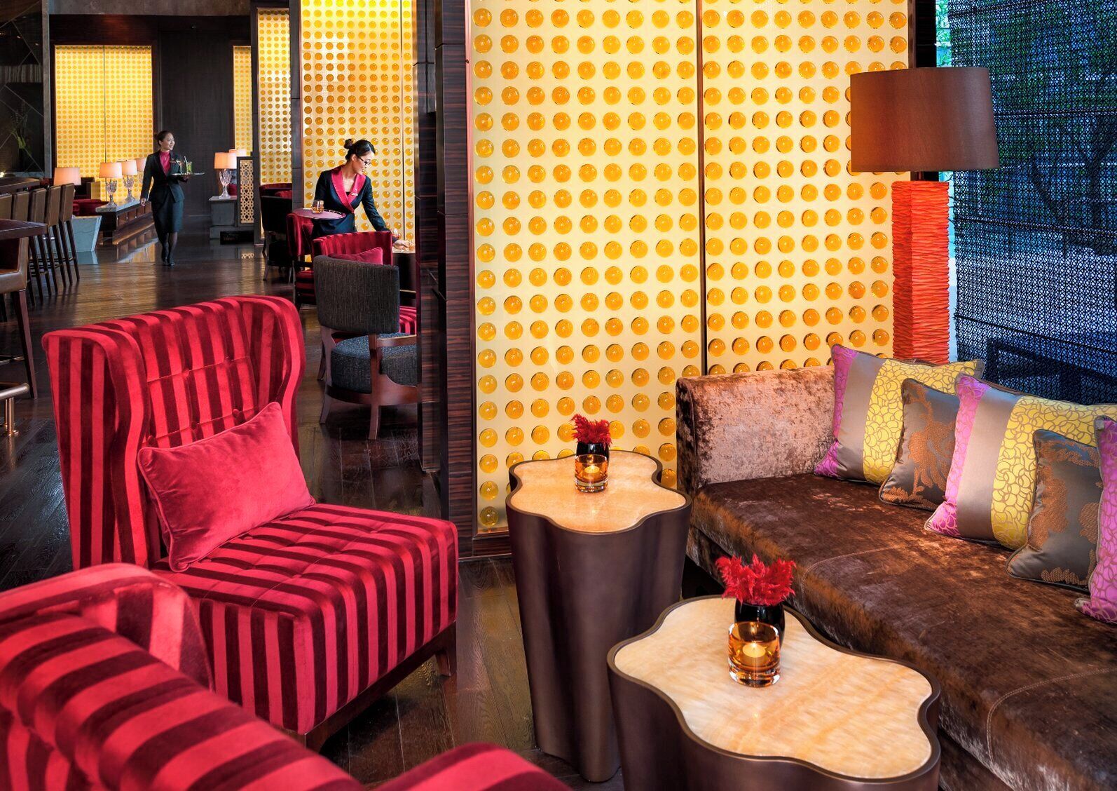 A modern lounge area with striped red sofas, a brown leather couch with colorful cushions, and a patterned yellow wall.