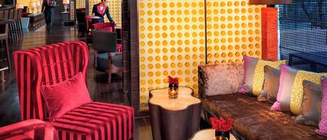 A modern lounge area with striped red sofas, a brown leather couch with colorful cushions, and a patterned yellow wall.