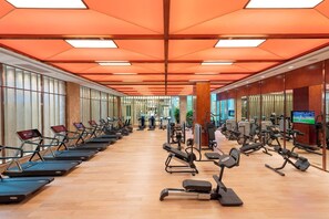 A gym with treadmills, elliptical machines, and weight machines arranged in rows.