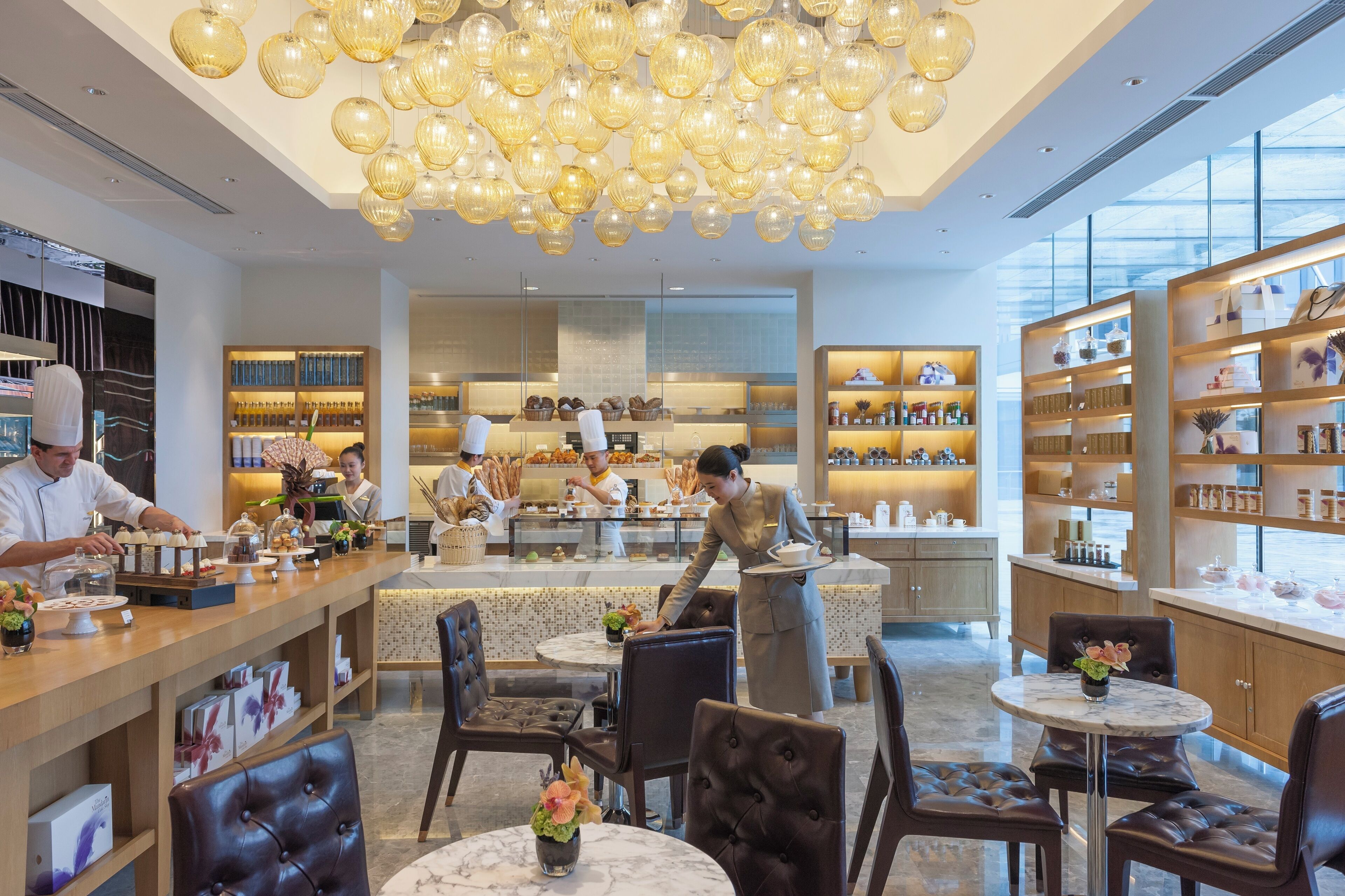 A modern restaurant with a central bar area, seating with round tables, and a ceiling adorned with spherical light fixtures.