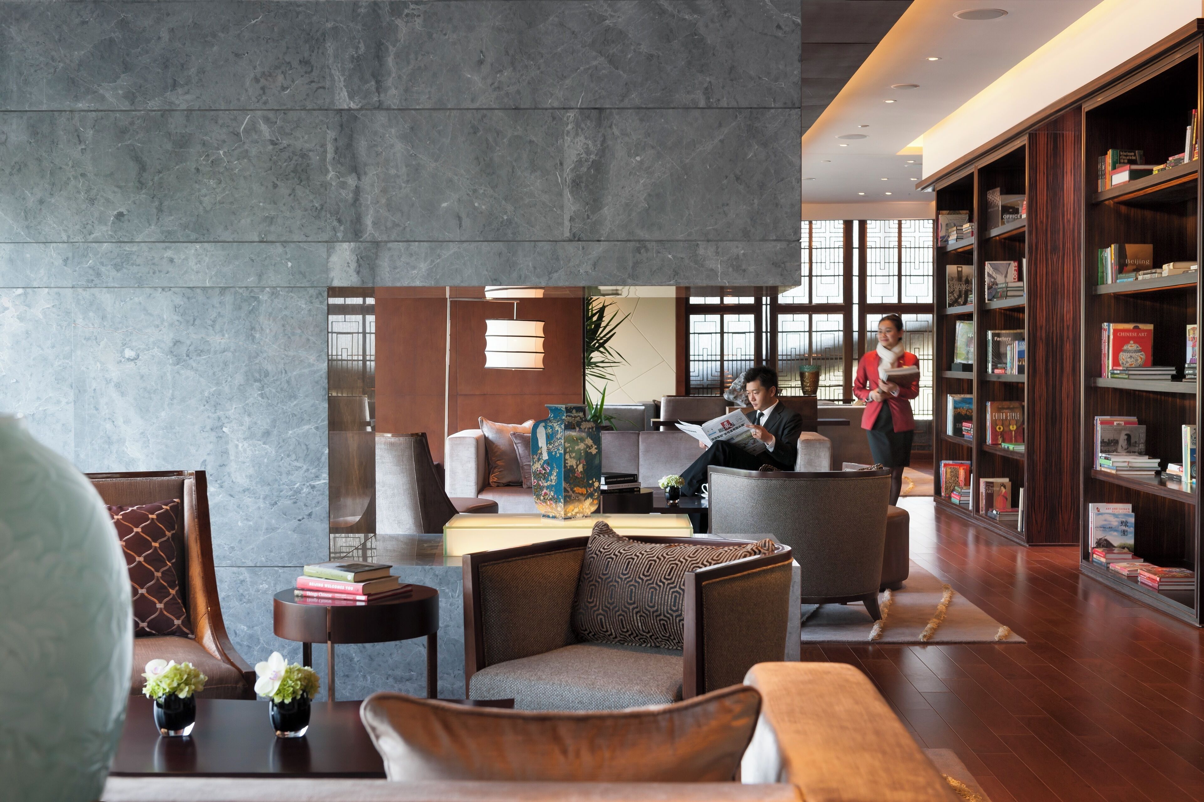 A modern lobby with seating areas, a large bookshelf, and a reception desk.