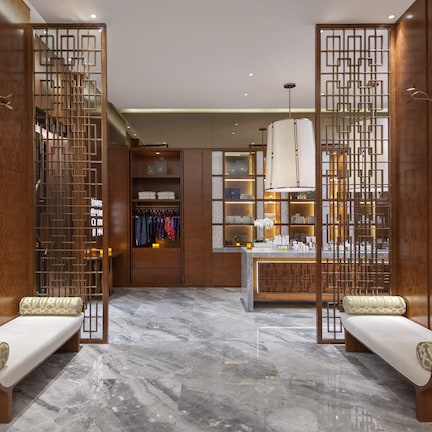 A modern hotel lobby with a marble floor, wooden benches, a reception desk, and a clothing store.
