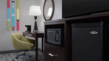 A hotel room with a microwave, refrigerator, desk, chair, lamp, and a wall with colorful vertical blinds.