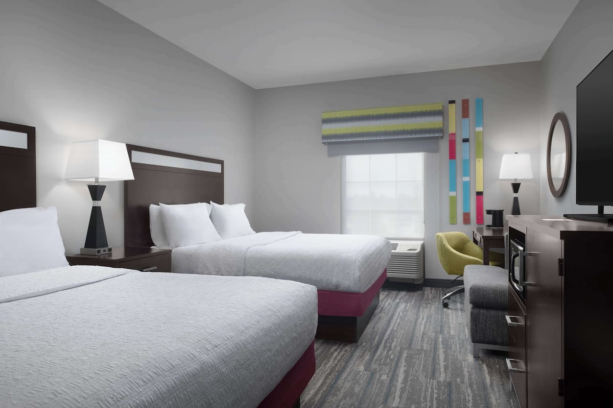 A hotel room with two beds, a desk with a computer, a chair, a TV, and a window with a view.