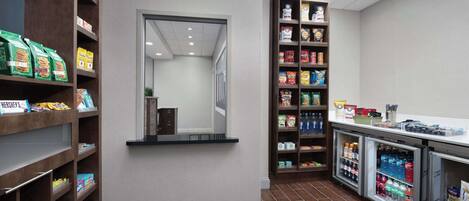 Eine saubere, übersichtliche Snackbar mit Regalen voller verschiedener Snacks und Getränke, sowie einem Kühlschrank voller Erfrischungen.