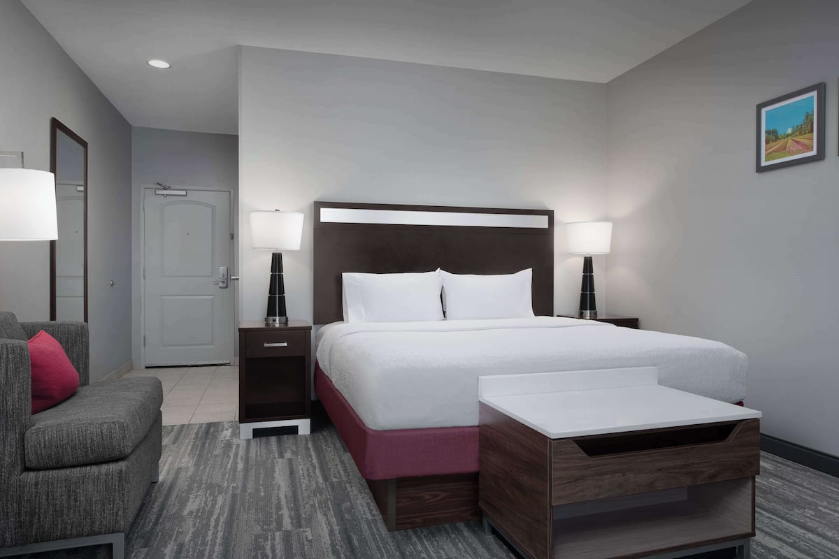 A hotel room with a bed, bedside tables, a nightstand, a chair, and a small table.
