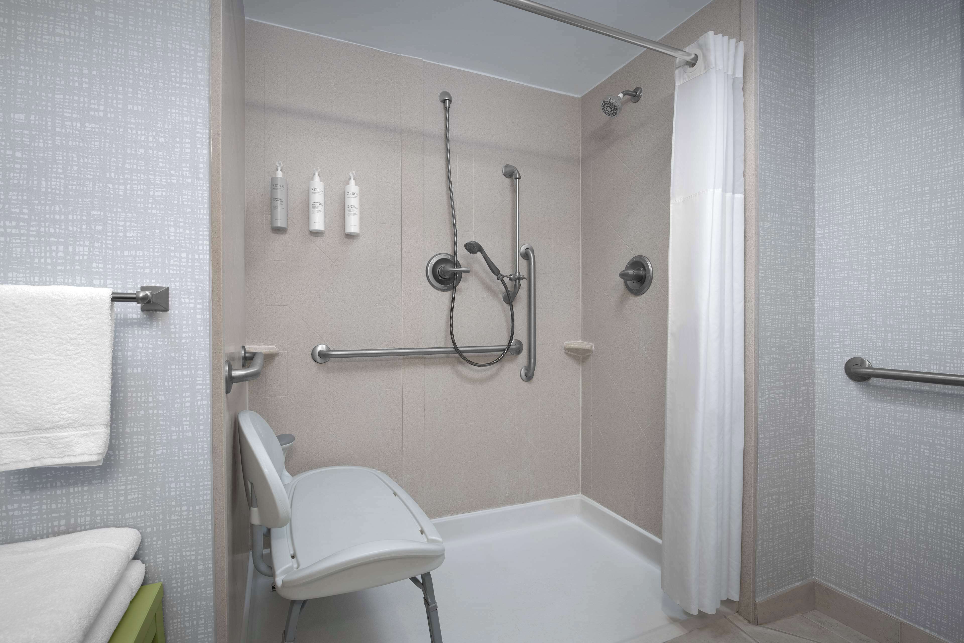 A modern bathroom with a walk-in shower, grab bars, a white toilet, and a green bench.