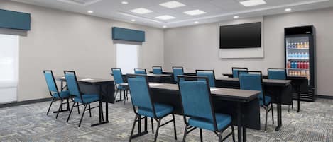 A conference room with a large table, chairs, a flat-screen TV, and a beverage refrigerator.