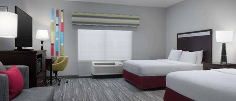 Habitación de hotel con dos camas, un escritorio, una silla, un televisor y una ventana con persianas.
