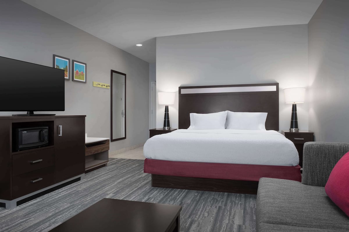 A modern hotel room with a large bed, a flat-screen TV, a desk, and a chair.