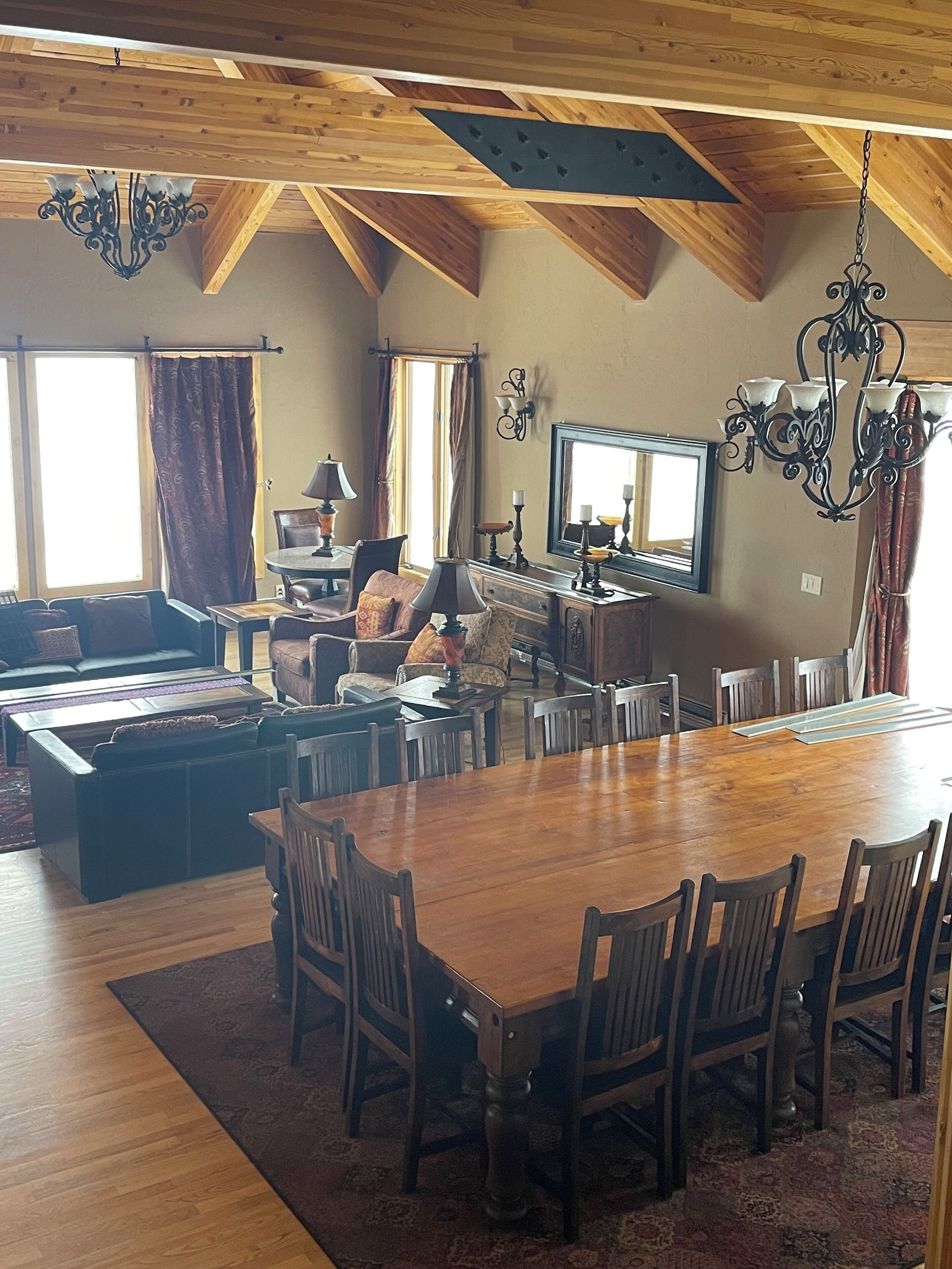 A spacious dining area with a large wooden table surrounded by chairs, a sofa, and a television.