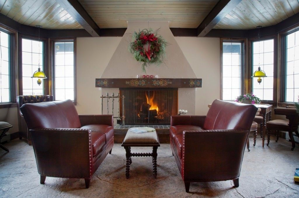 A cozy room with leather armchairs, a fireplace with a wreath, and large windows.