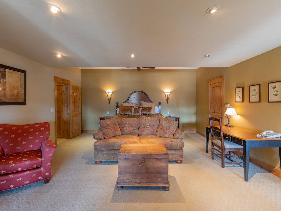 Una sala de estar acogedora con un sofá, un sillón rojo, una mesa de centro de madera y un escritorio con una lámpara.