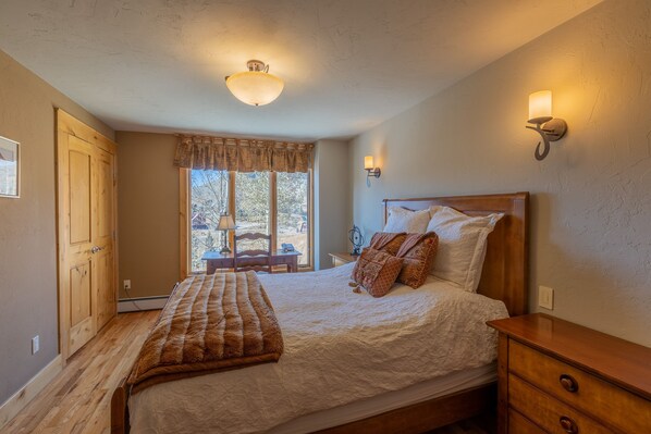A bedroom with a wooden bed, a nightstand, a lamp, and a window with a view of the outdoors. - Nordic Inn (Crested Butte)