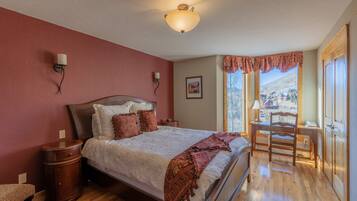 A bedroom with a bed, bedside tables, a desk with a chair, a window with a view, and a ceiling light.