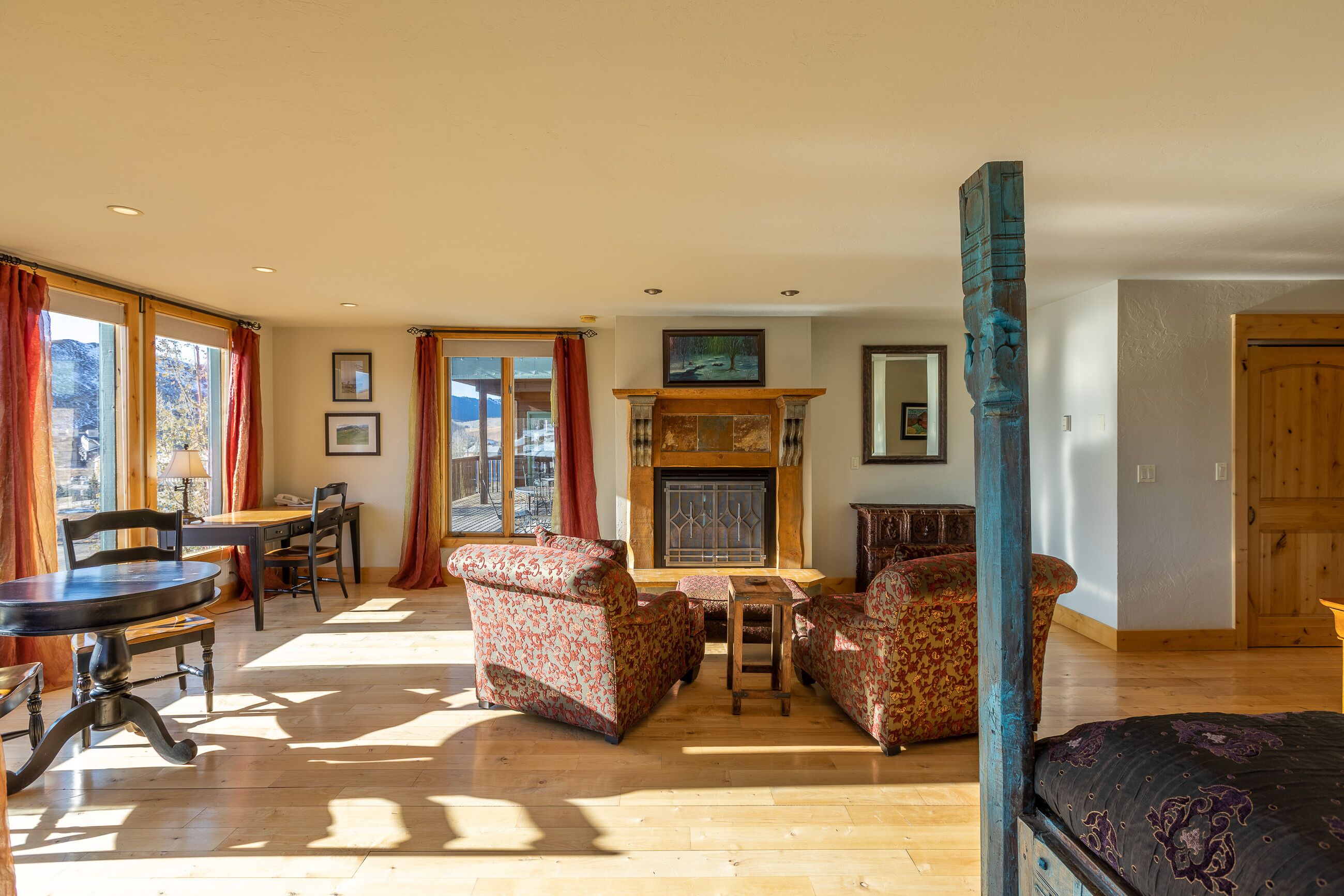 A spacious living room with a fireplace, wooden furniture, and large windows.