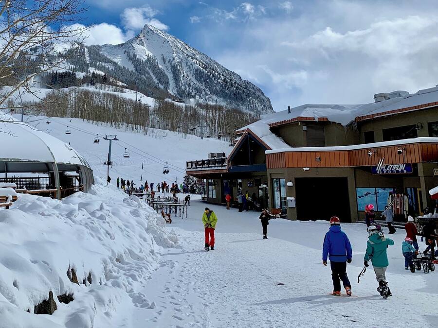 A ski resort with a mountain backdrop, a ski lift, and a building labeled "FLATIRON SPORTS".