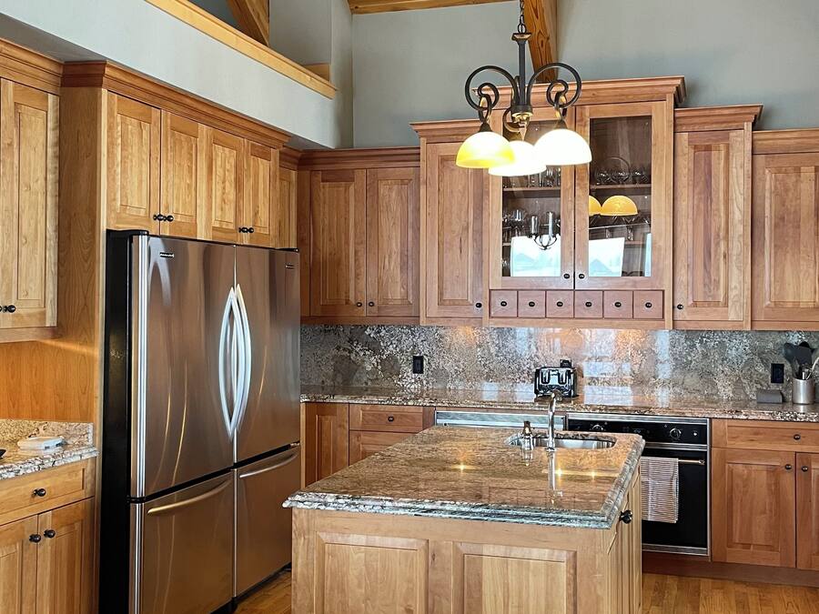 Una cocina amplia con armarios de madera, un refrigerador de acero inoxidable, encimeras de granito y una lámpara colgante.