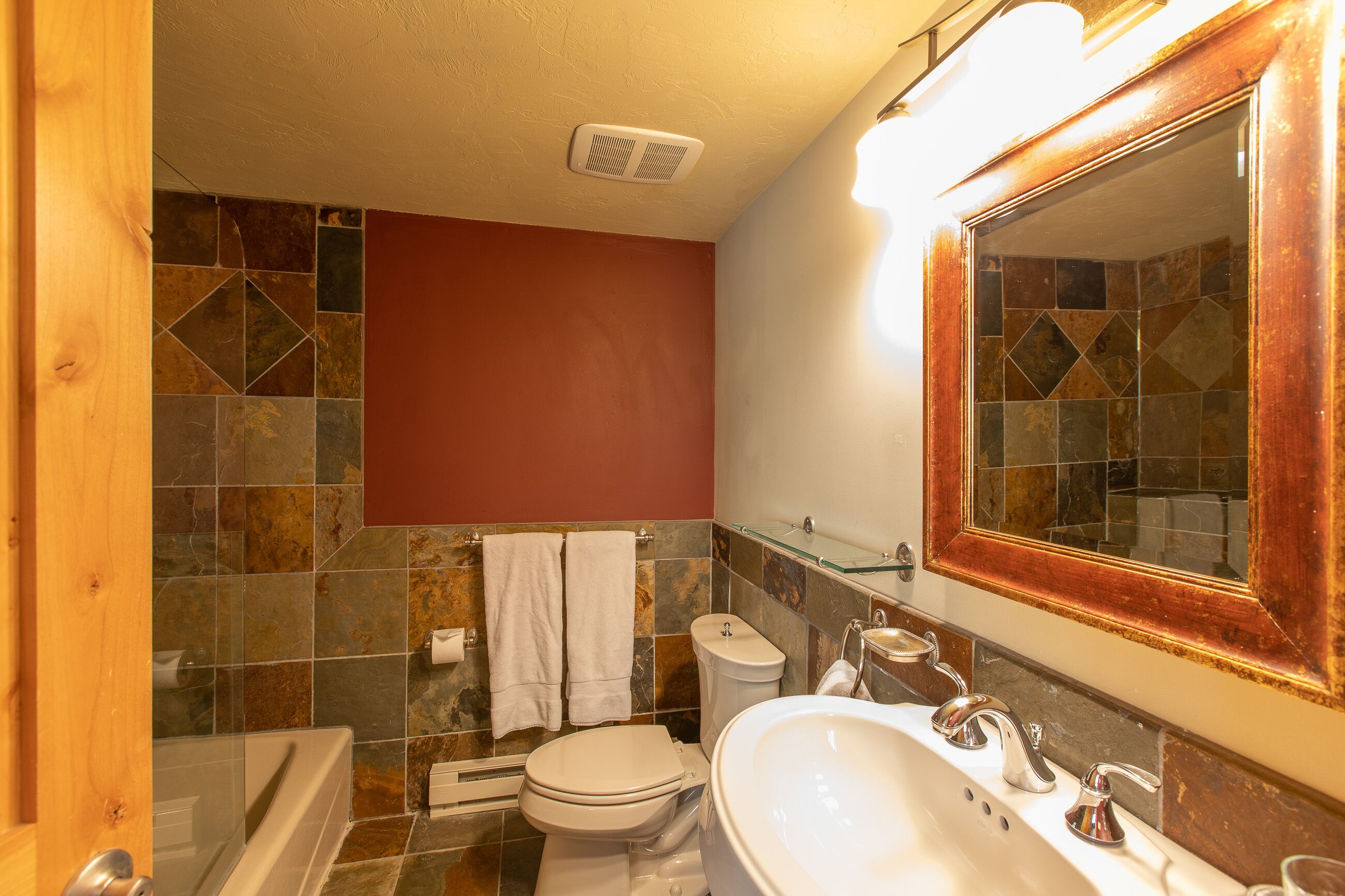 Un baño con bañera, inodoro, lavamanos y un espejo grande.