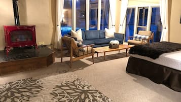 Una habitación acogedora con sofá, sillas, una mesita de centro, cama, chimenea y ventanas amplias.
