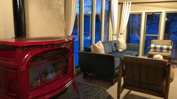 Ein gemütliches Wohnzimmer mit einem roten Kaminofen, einem blauen Sofa und einem Korbstuhl.
