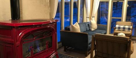 En hyggelig stue med en rød brændeovn, en blå sofa og en fletstol.