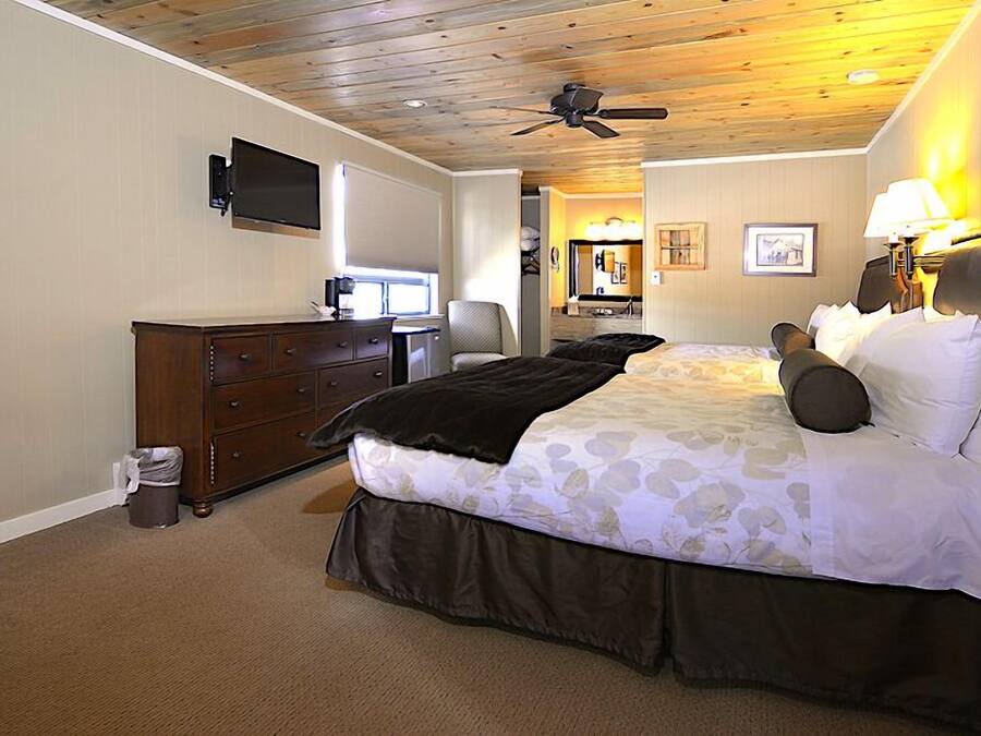 A bedroom with a bed, dresser, television, ceiling fan, and a small desk with chair.