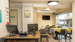 A hotel reception area with two computer workstations, a fire exit sign, a menu board, and a view of the street through large windows. - Septimum (Istanbul)