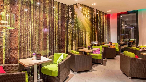 Un espace intérieur moderne, doté de meubles en osier, d’un mur décoré sur le thème de la forêt et d’une cloison en verre.